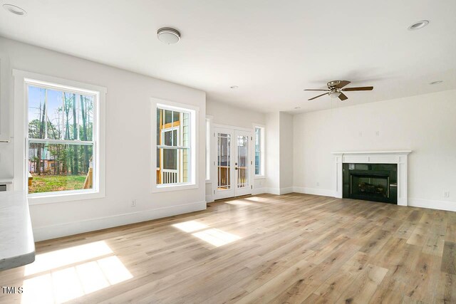 unfurnished living room featuring light hardwood / wood-style flooring, french doors, ceiling fan, and a healthy amount of sunlight