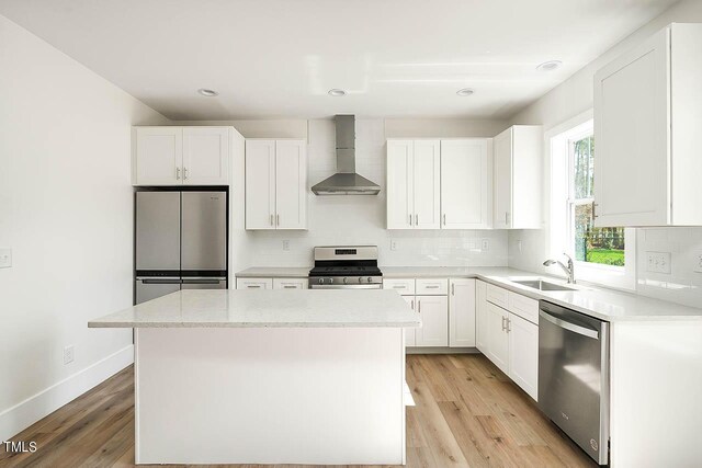 kitchen featuring a kitchen island, stainless steel appliances, wall chimney range hood, light wood-type flooring, and white cabinets