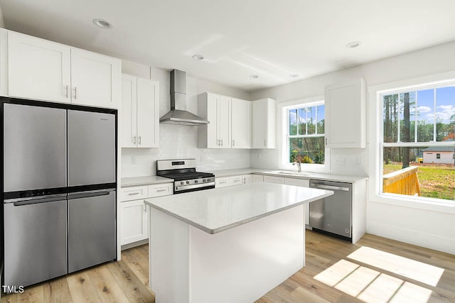 kitchen with wall chimney range hood, appliances with stainless steel finishes, white cabinetry, and light hardwood / wood-style floors