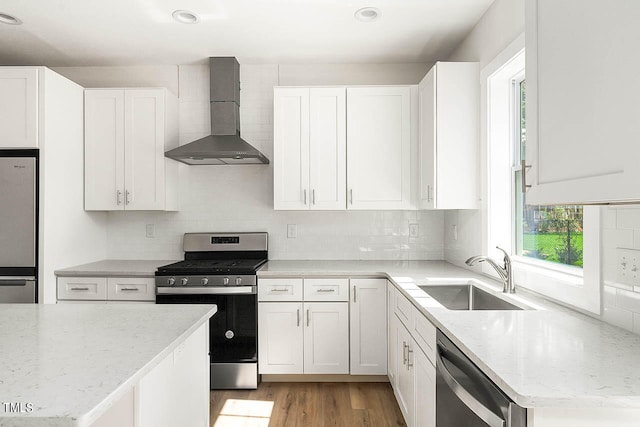 kitchen featuring a healthy amount of sunlight, stainless steel appliances, wall chimney range hood, and white cabinets