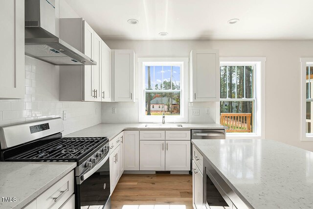 kitchen with wall chimney range hood, decorative backsplash, appliances with stainless steel finishes, white cabinets, and light hardwood / wood-style floors