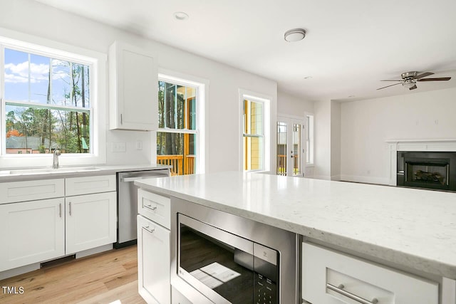 kitchen with stainless steel appliances, light stone countertops, ceiling fan, white cabinets, and light hardwood / wood-style floors