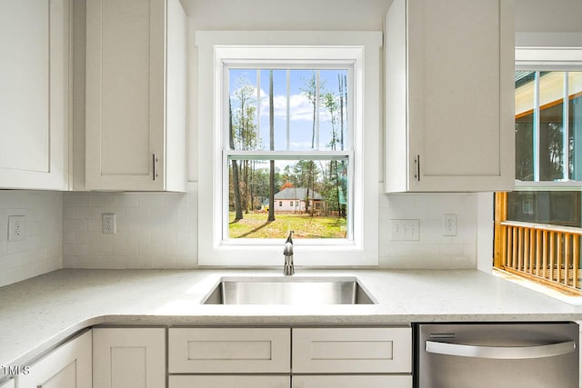 kitchen featuring stainless steel dishwasher, light stone counters, sink, and decorative backsplash