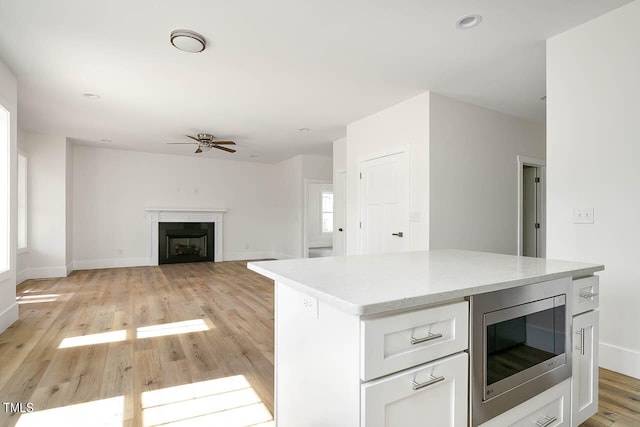 kitchen with light hardwood / wood-style floors, ceiling fan, stainless steel microwave, and white cabinets