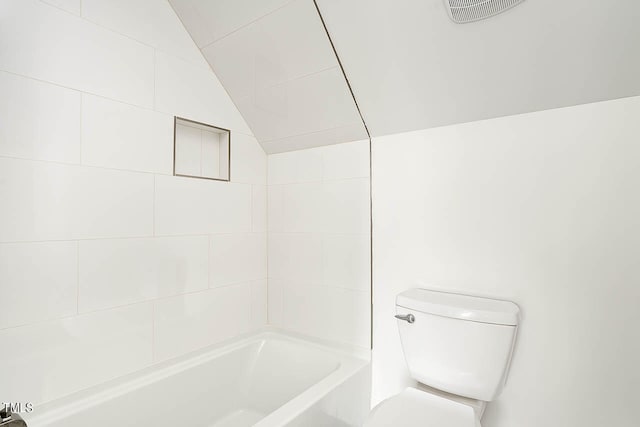 bathroom featuring tiled shower / bath, vaulted ceiling, and toilet