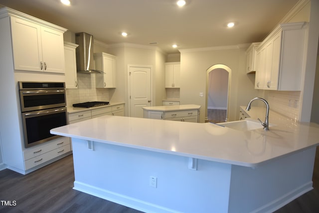 kitchen featuring double oven, dark wood-type flooring, a sink, wall chimney range hood, and a peninsula