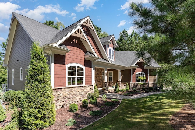 craftsman house featuring a front yard, stone siding, and roof with shingles