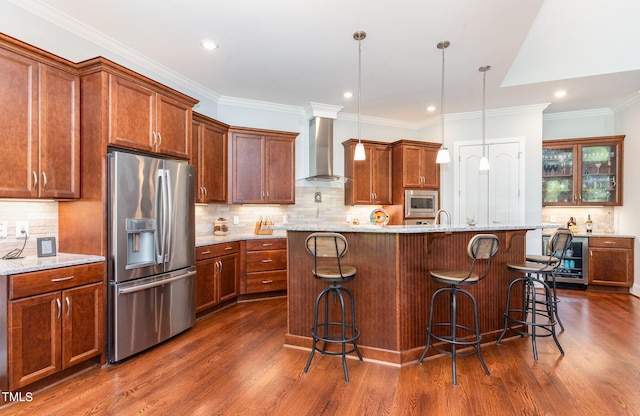 kitchen with hanging light fixtures, appliances with stainless steel finishes, wall chimney range hood, dark wood-type flooring, and a kitchen breakfast bar