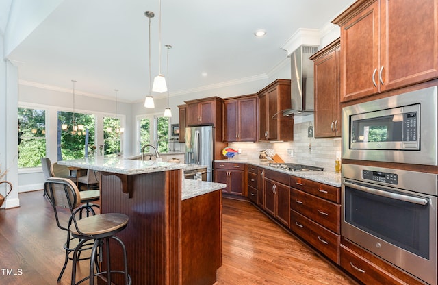 kitchen with hanging light fixtures, wood-type flooring, stainless steel appliances, and wall chimney range hood