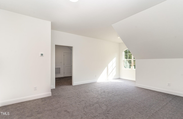 additional living space with dark colored carpet and vaulted ceiling