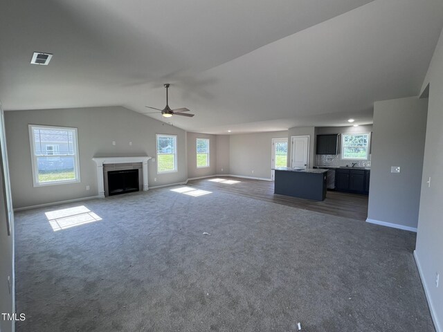 unfurnished living room with ceiling fan, dark colored carpet, and vaulted ceiling