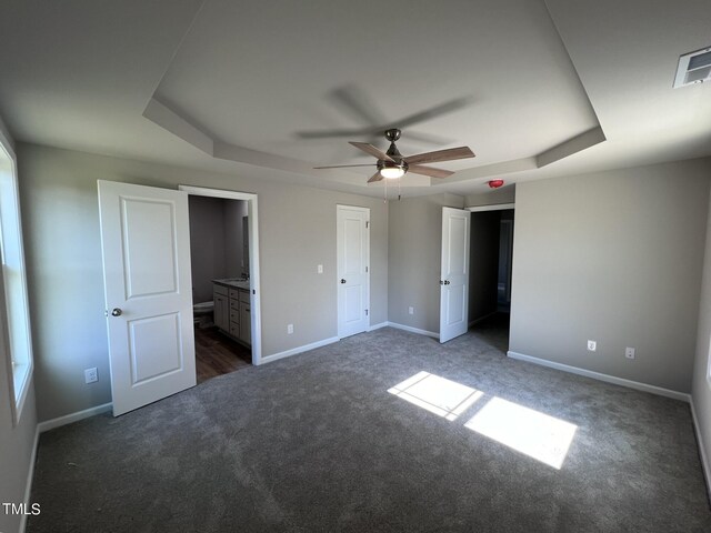 unfurnished bedroom featuring carpet flooring, ensuite bath, a tray ceiling, and ceiling fan