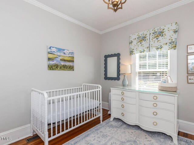 bedroom with a nursery area, ornamental molding, and wood-type flooring