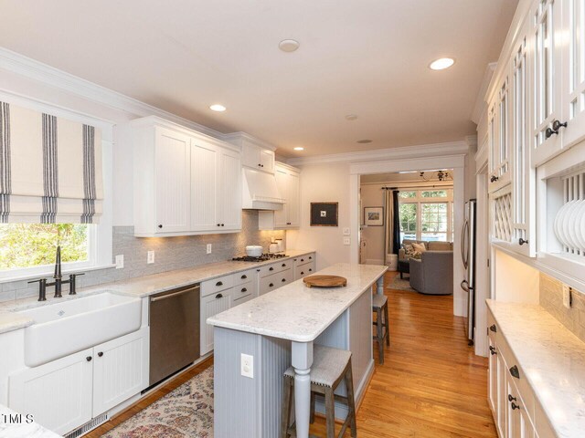 kitchen with light wood-type flooring, stainless steel appliances, white cabinetry, a kitchen bar, and a kitchen island