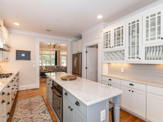 kitchen with white cabinetry, light hardwood / wood-style flooring, backsplash, a kitchen island, and appliances with stainless steel finishes