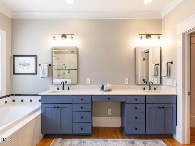 bathroom featuring wood-type flooring, a relaxing tiled tub, ornamental molding, and vanity