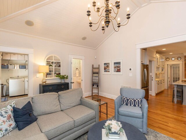 living room with an inviting chandelier, light hardwood / wood-style floors, separate washer and dryer, high vaulted ceiling, and ornamental molding