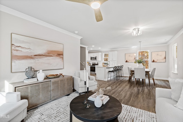 living room featuring ceiling fan, sink, light wood-type flooring, and crown molding