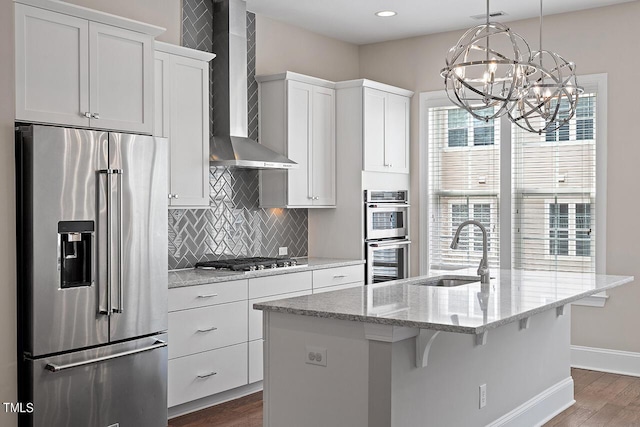 kitchen with stainless steel appliances, tasteful backsplash, a sink, wall chimney range hood, and a notable chandelier