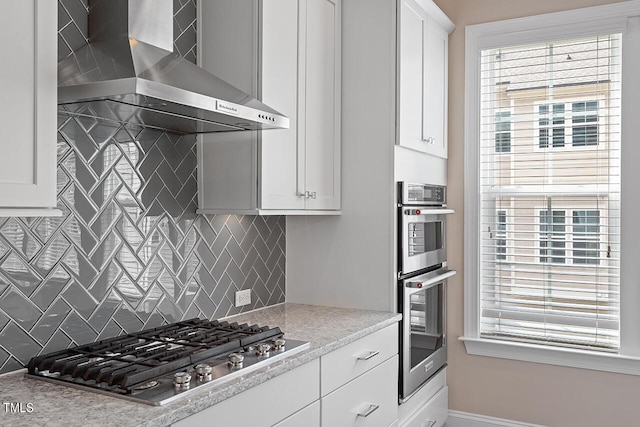 kitchen with wall chimney range hood, white cabinetry, appliances with stainless steel finishes, and decorative backsplash