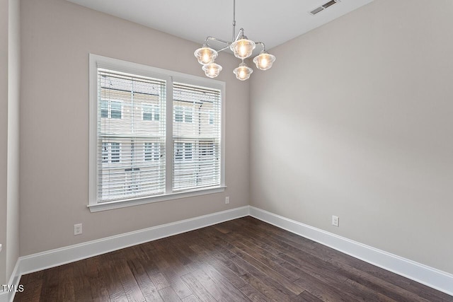 empty room with dark wood-style flooring, a notable chandelier, baseboards, and visible vents