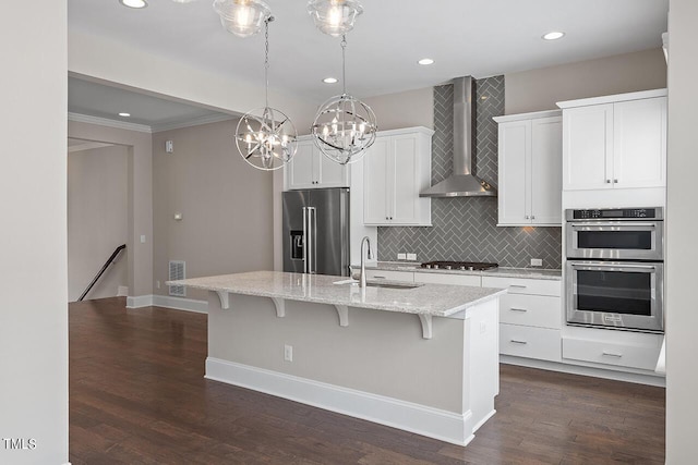 kitchen featuring a kitchen bar, a sink, wall chimney range hood, a kitchen island with sink, and appliances with stainless steel finishes