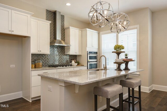 kitchen featuring white cabinetry, gas cooktop, decorative backsplash, double oven, and wall chimney range hood
