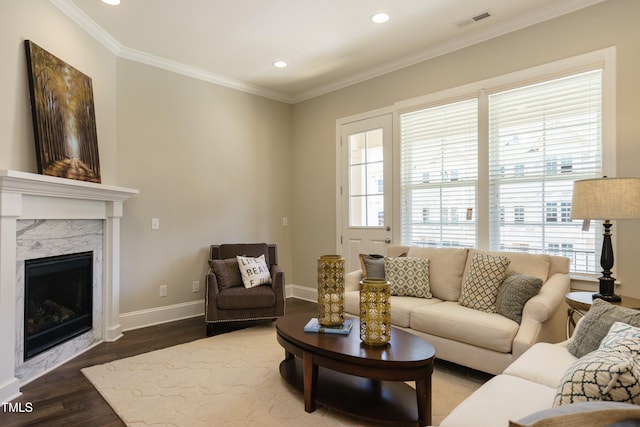 living room featuring visible vents, a premium fireplace, baseboards, ornamental molding, and wood finished floors