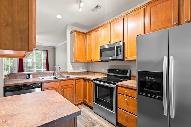 kitchen with kitchen peninsula, sink, crown molding, appliances with stainless steel finishes, and light hardwood / wood-style floors