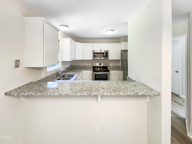 kitchen featuring hardwood / wood-style floors, stainless steel appliances, sink, kitchen peninsula, and white cabinetry