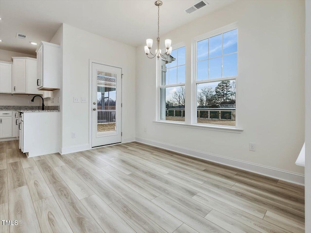 unfurnished dining area with a notable chandelier, visible vents, light wood finished floors, and baseboards