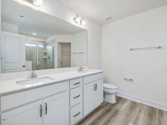 full bath with visible vents, a stall shower, wood finished floors, and a sink