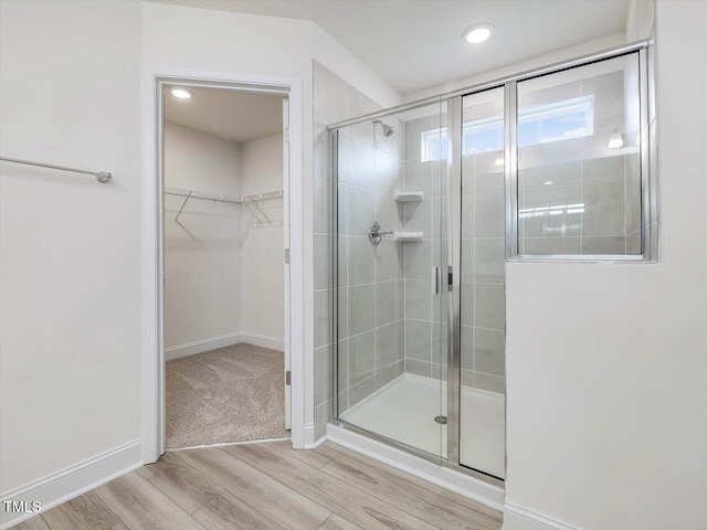 full bathroom with a shower stall, a walk in closet, baseboards, and wood finished floors