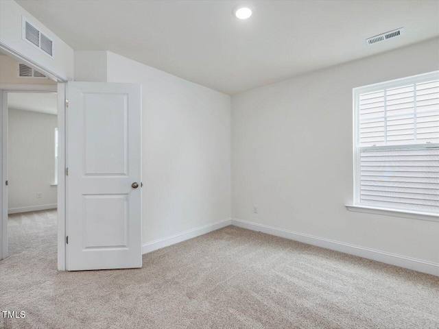 spare room featuring light colored carpet, visible vents, and baseboards