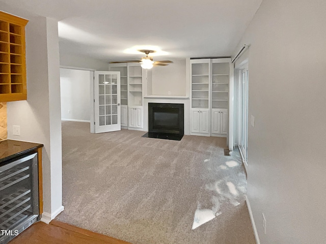 unfurnished living room with carpet, baseboards, a fireplace with flush hearth, ceiling fan, and wine cooler