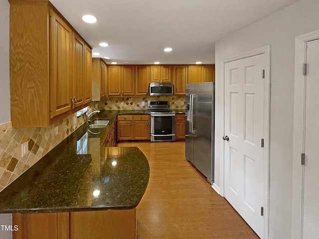 kitchen featuring brown cabinetry, stainless steel appliances, dark stone counters, and a sink