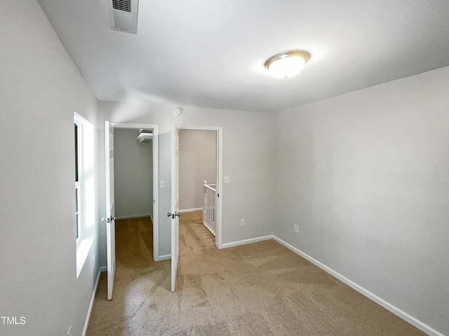 unfurnished bedroom with visible vents, a walk in closet, baseboards, light colored carpet, and a closet