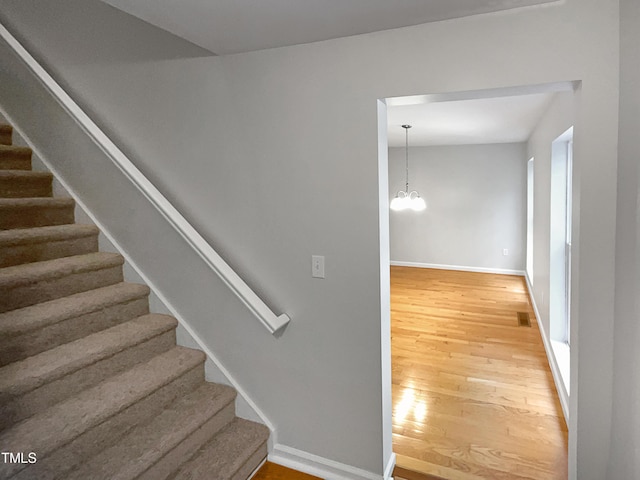 stairs with a notable chandelier, visible vents, baseboards, and wood finished floors