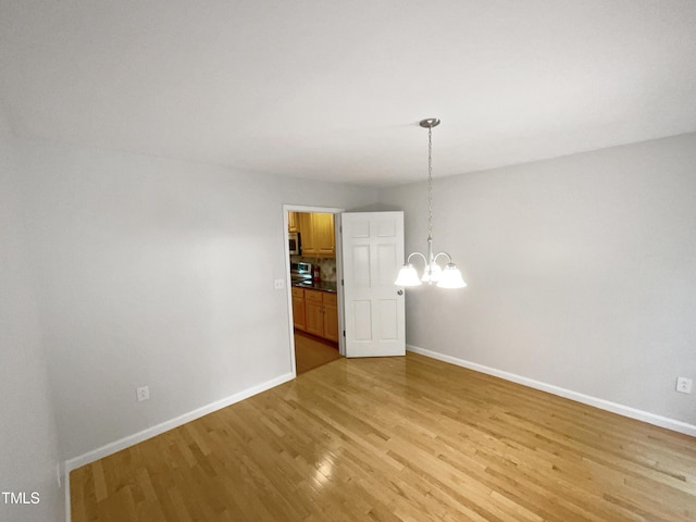 empty room featuring light wood finished floors, a notable chandelier, and baseboards