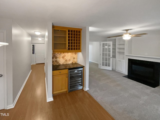 bar with a fireplace with flush hearth, beverage cooler, wood finished floors, decorative backsplash, and baseboards