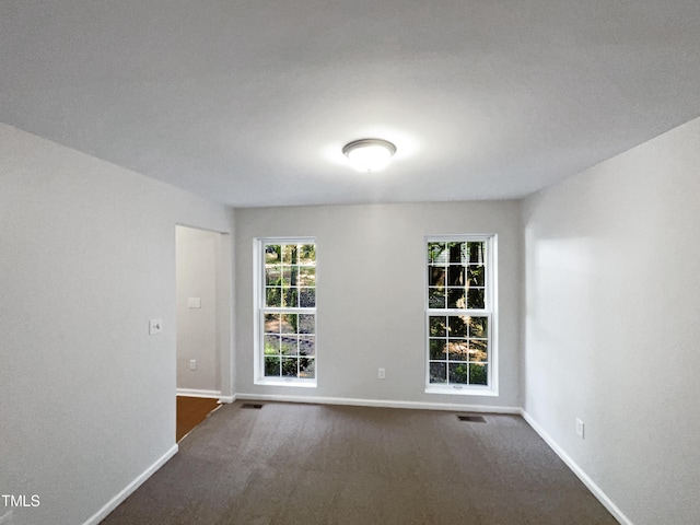 unfurnished room featuring visible vents, baseboards, and dark colored carpet