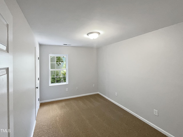 spare room with baseboards and dark carpet