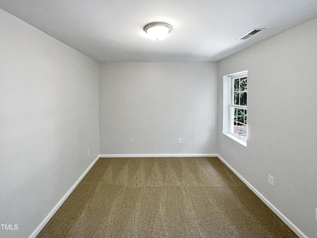 spare room featuring baseboards, visible vents, and dark colored carpet