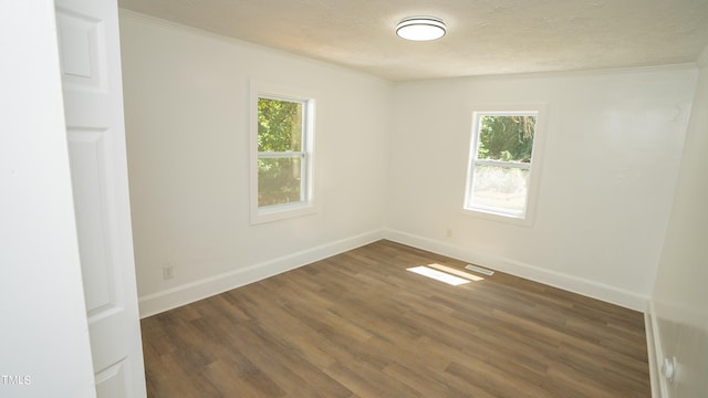 empty room with crown molding, dark wood-type flooring, and a wealth of natural light