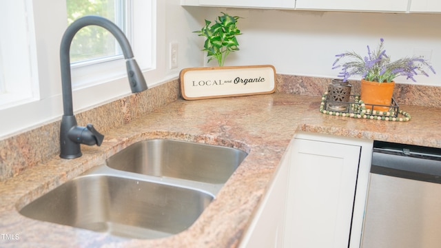 interior details featuring stainless steel dishwasher, white cabinetry, sink, and light stone counters