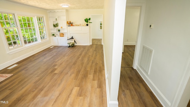 hall with built in shelves, a textured ceiling, crown molding, and hardwood / wood-style floors