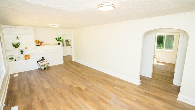 unfurnished living room with a textured ceiling, light hardwood / wood-style floors, and ornamental molding