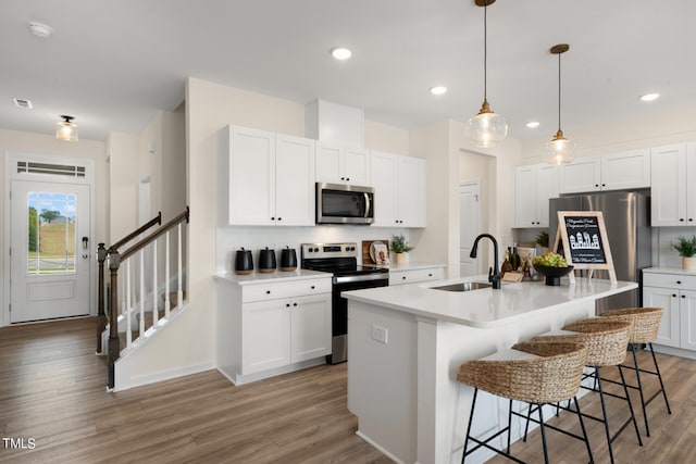 kitchen with a center island with sink, stainless steel appliances, sink, white cabinetry, and light wood-type flooring