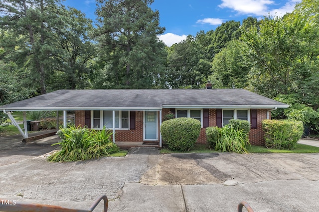 ranch-style home with a carport, brick siding, covered porch, and driveway