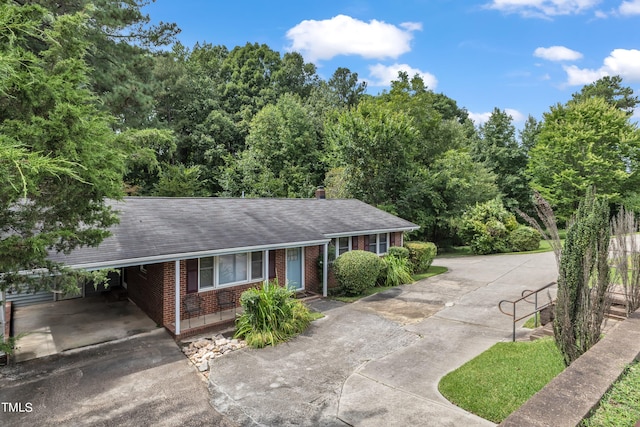 ranch-style home with a carport, brick siding, driveway, and a shingled roof